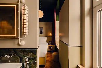 Blick vom Badezimmer in ein Hotelzimmer mit grünem Marmorwaschbecken, warmer Beleuchtung und Bett im Hintergrund.