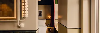 Blick vom Badezimmer in ein Hotelzimmer mit grünem Marmorwaschbecken, warmer Beleuchtung und Bett im Hintergrund.