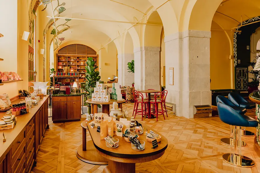 Warm lounge and market area with arches, high ceilings, wood flooring, shelving, and colorful seating.