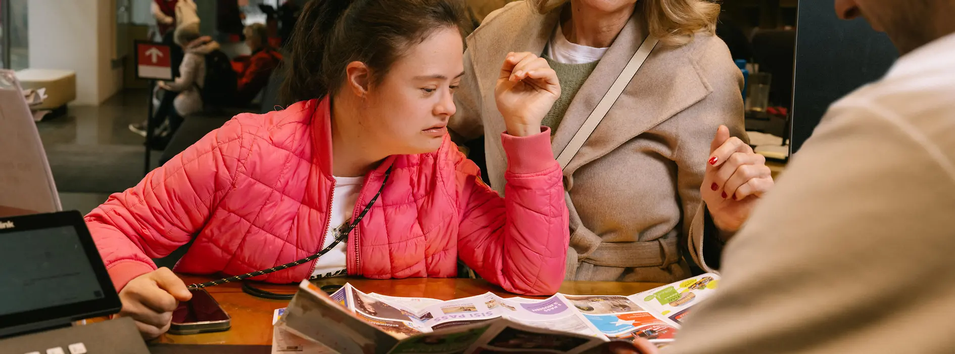 Zwei Besucherinnen lassen sich an einem Schalter der Tourist-Info beraten. Gemeinsam schauen sie mit einem Mitarbeiter auf einen aufgeklappten Stadtplan.