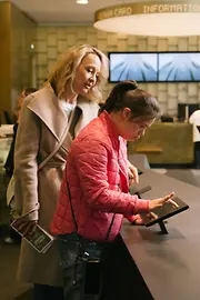 Zwei Besucherinnen nutzen in der Tourist-Info Albertinaplatz einen digitalen Informationstisch. Das Bild zeigt einen barrierearmen Zugang zu touristischen Informationen.
