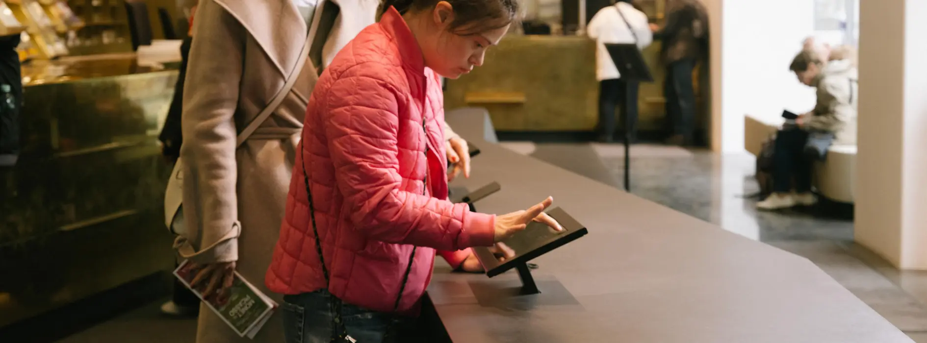 Zwei Besucherinnen nutzen in der Tourist-Info Albertinaplatz einen digitalen Informationstisch. Das Bild zeigt einen barrierearmen Zugang zu touristischen Informationen.