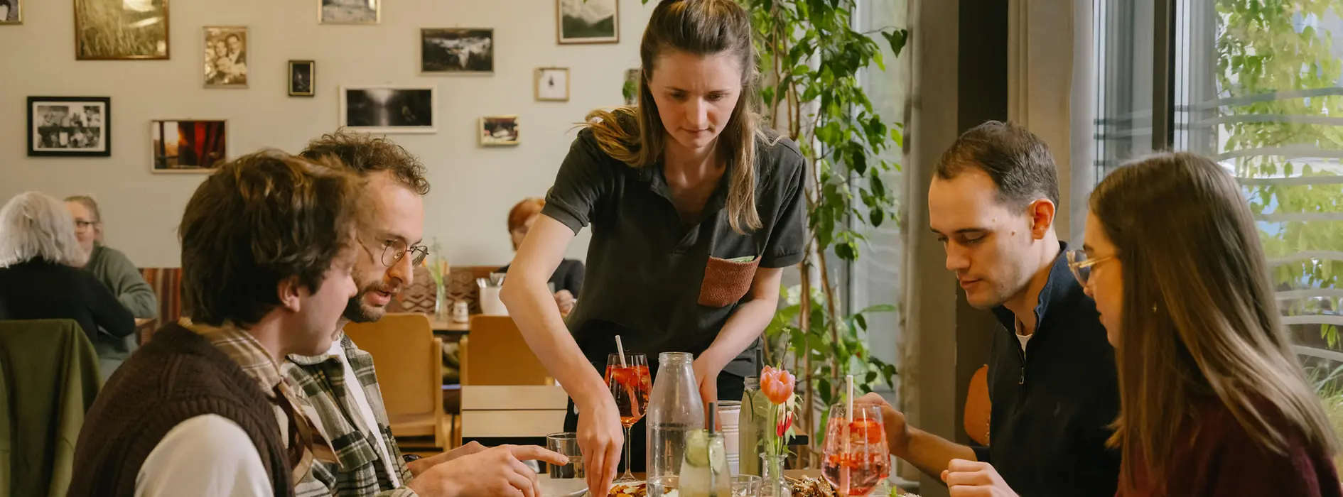 Guests are sitting together at a table at magdas Lokal, including a man using a wheelchair. The image shows an inclusive and accessible restaurant setting.