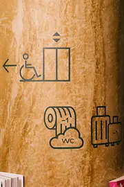 Eine Säule im magdas Lokal zeigt Piktogramme für barrierefreien Zugang mit Lift, WC und Gepäckaufbewahrung. Die Symbole dienen der Orientierung im Innenraum.