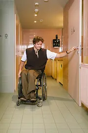 A man using a wheelchair opens the door to an accessible restroom at magdas Lokal. The image shows independent access to sanitary facilities.