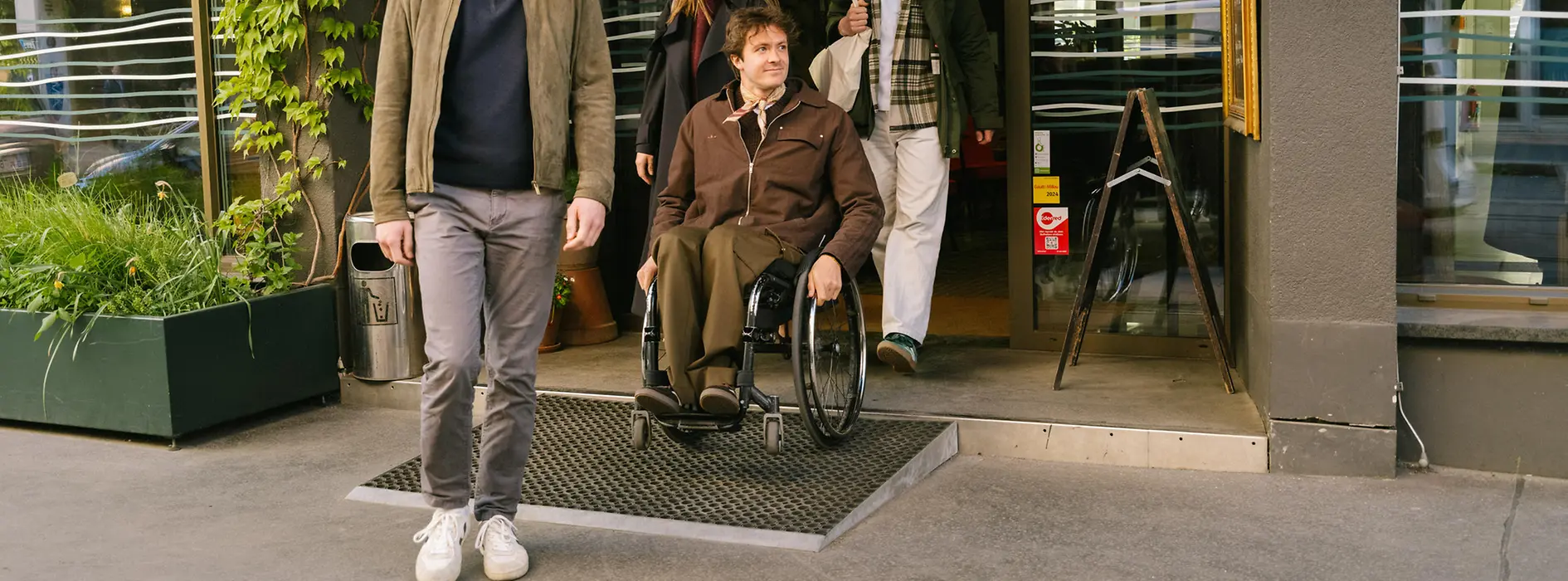 Several guests are leaving magdas Lokal, including a man using a wheelchair on a ramp at the entrance. The image shows accessible access to the venue.