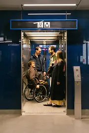 Several people, including a man using a wheelchair, are using an elevator at a Wiener Linien station. The image shows accessible circulation with an elevator.