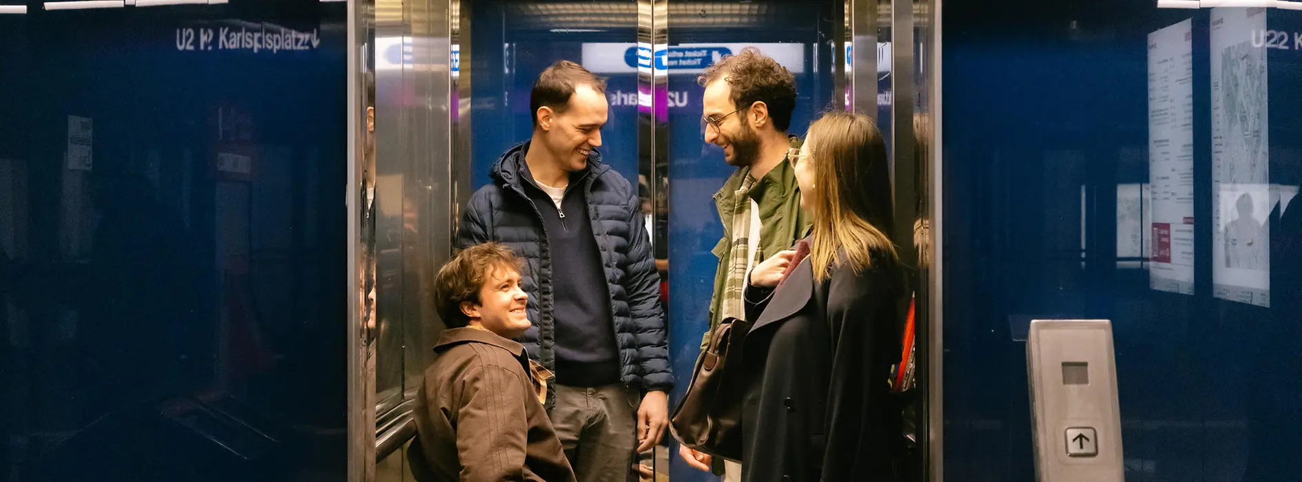 Several people, including a man using a wheelchair, are using an elevator at a Wiener Linien station. The image shows accessible circulation with an elevator.