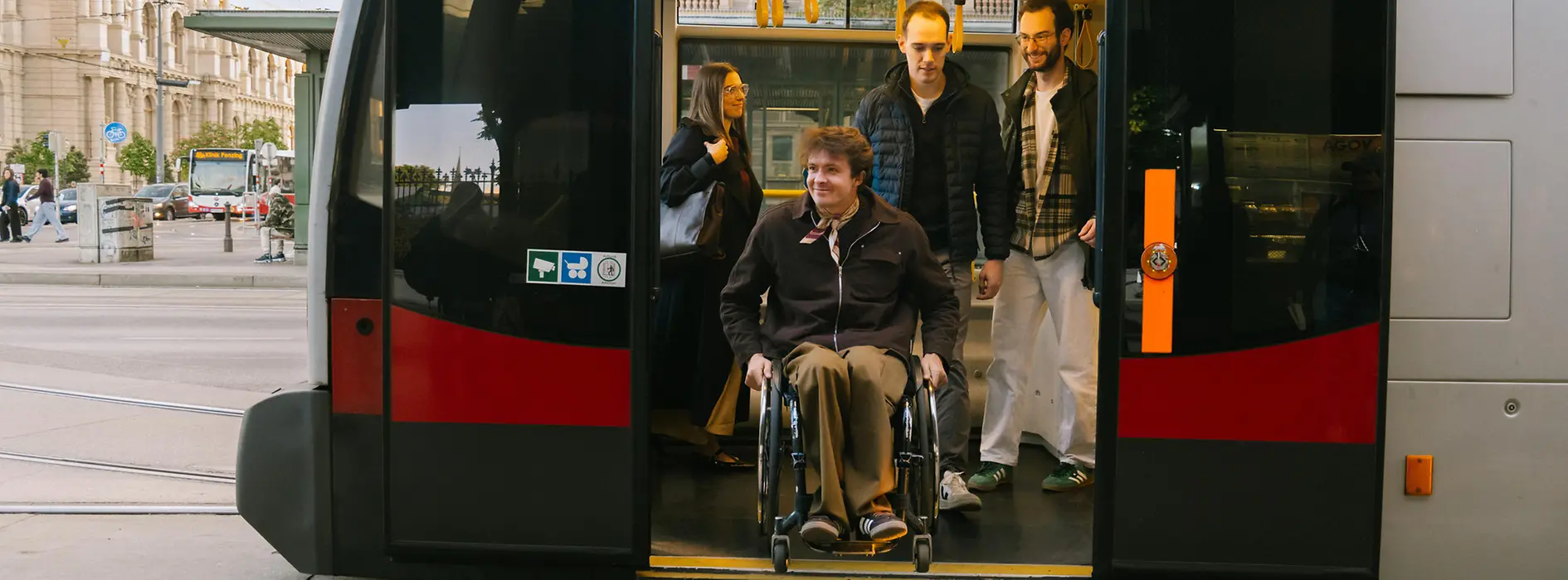 Ein Mann im Rollstuhl fährt aus einer Straßenbahn der Wiener Linien aus, während weitere Fahrgäste im Fahrzeug stehen. Das Bild zeigt barrierefreie Mobilität im öffentlichen Verkehr.