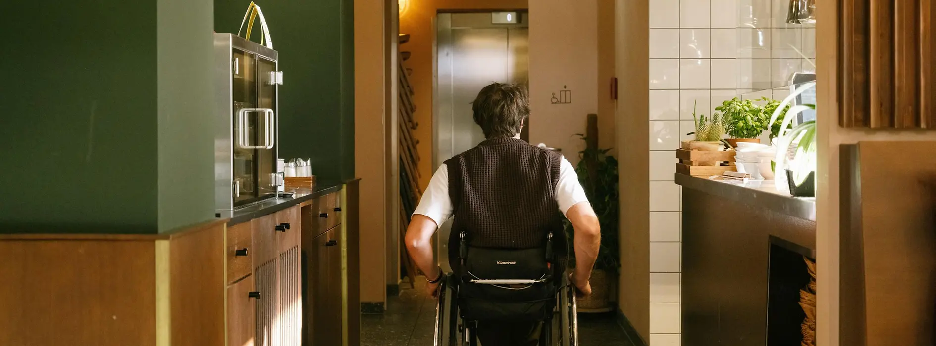 A man using a wheelchair is moving through the interior of magdas Lokal towards an elevator. The image shows accessible wayfinding inside the venue.