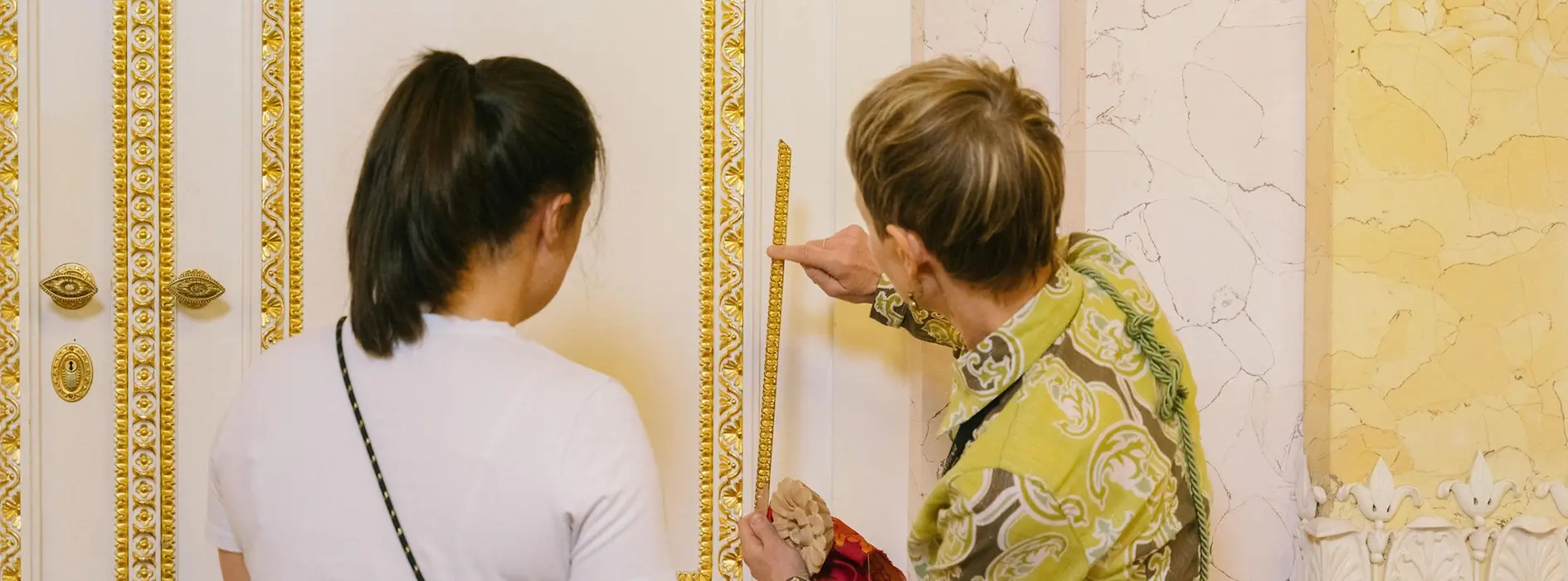 Zwei Personen stehen in der Albertina vor einer verzierten Wand oder einem Exponat, eine Person zeigt auf ein Detail. Das Bild zeigt barrierearme, unterstützende Vermittlung im Ausstellungsraum.