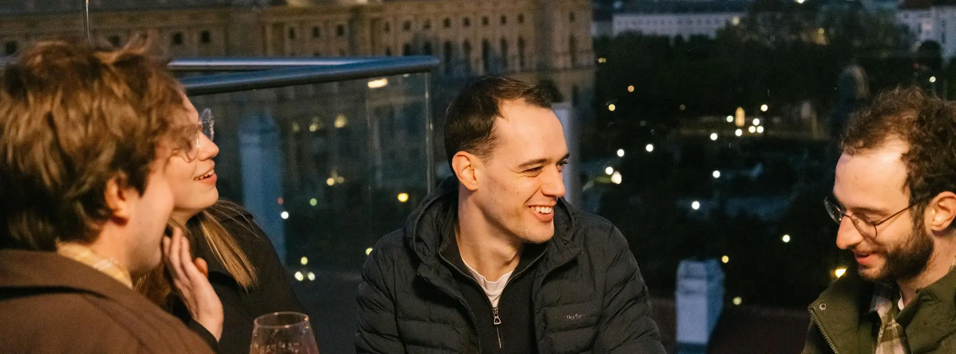 Mehrere Personen sitzen gemeinsam auf der Terrasse der MQ Libelle, darunter ein Mann im Rollstuhl, mit Blick über die Stadt. 