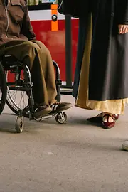 Zu sehen sind die Füße mehrerer Personen am Straßenbahnsteig, darunter ein Rollstuhl. Das Bild zeigt barrierefreie Nutzung des öffentlichen Verkehrs im Alltag.