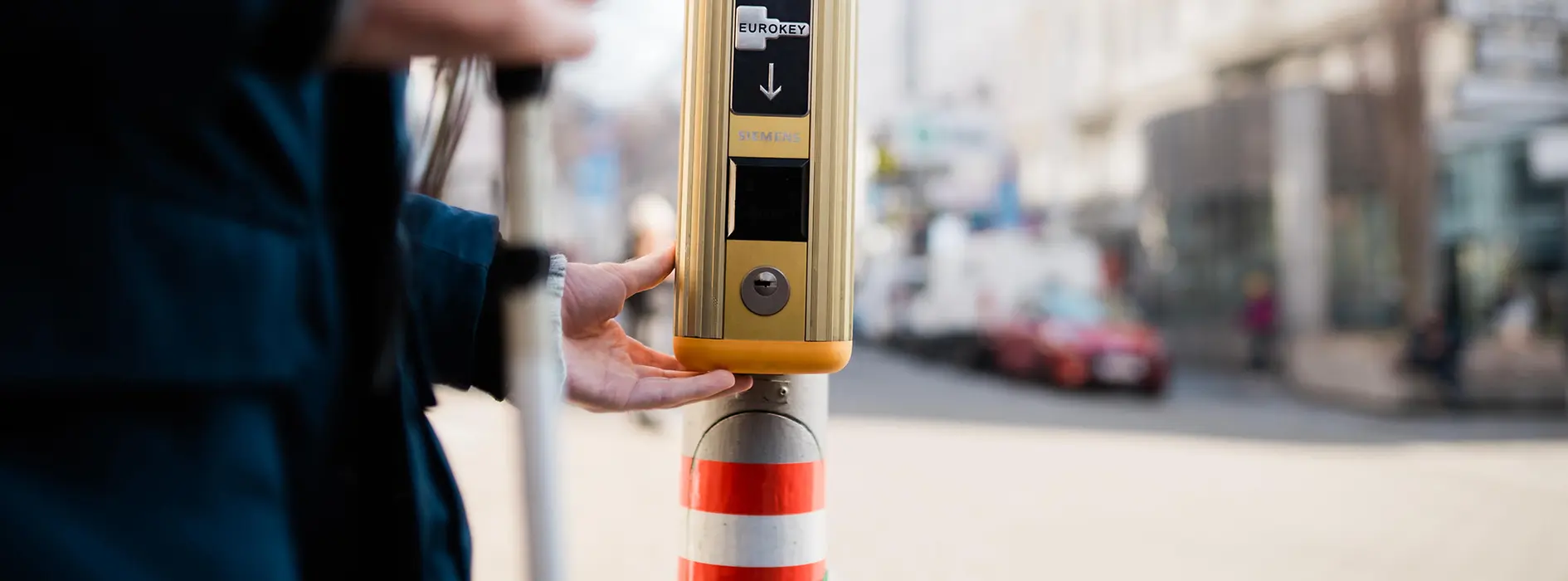 Eine Hand drückt eine Anforderungstaste an einer Haltestelle. Das Bild zeigt barrierefreie Unterstützung beim Ein- und Ausstieg im öffentlichen Verkehr.