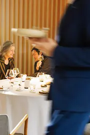Gäste sitzen an einem gedeckten Tisch im Restaurant Steirereck, während ein Mitarbeiter einen Teller serviert. Das Bild zeigt eine elegante Fine-Dining-Situation im Gastraum.