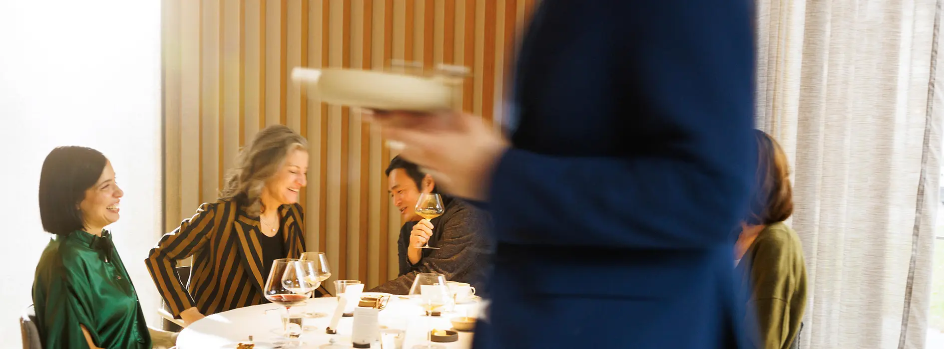 Gäste sitzen an einem gedeckten Tisch im Restaurant Steirereck, während ein Mitarbeiter einen Teller serviert. Das Bild zeigt eine elegante Fine-Dining-Situation im Gastraum.