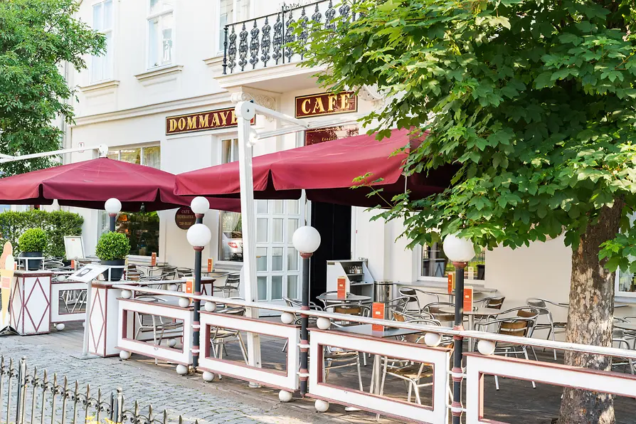 Café Dommayer outdoor seating area with red umbrellas and tables.