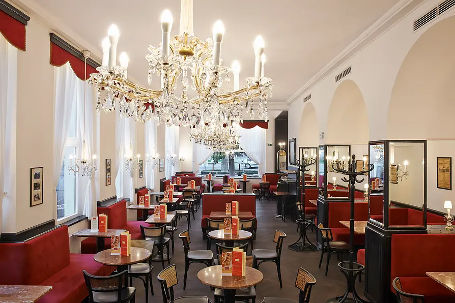 Interior of Café Dommayer with red banquettes and crystal chandeliers.