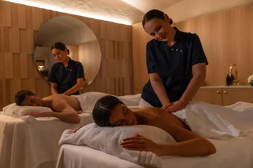 Two spa therapists massaging two guests in a treatment room at Anantara Palais Hansen Vienna.