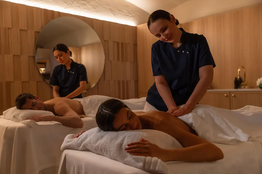 Two spa therapists massaging two guests in a treatment room at Anantara Palais Hansen Vienna.