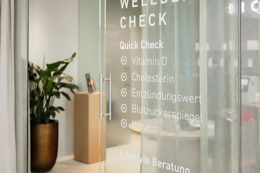 Glass door to the BIOGENA Wellbeing Check with information about health analyses and lifestyle consultation.