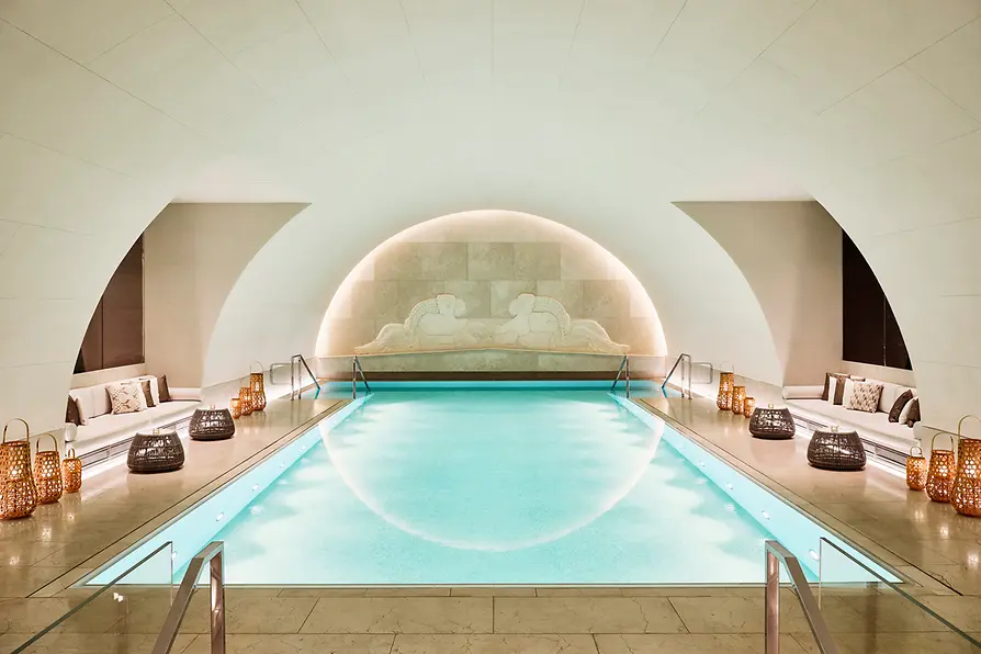 Pool area in the Arany Spa at Park Hyatt Vienna with an illuminated indoor pool, benches and decorative lanterns.
