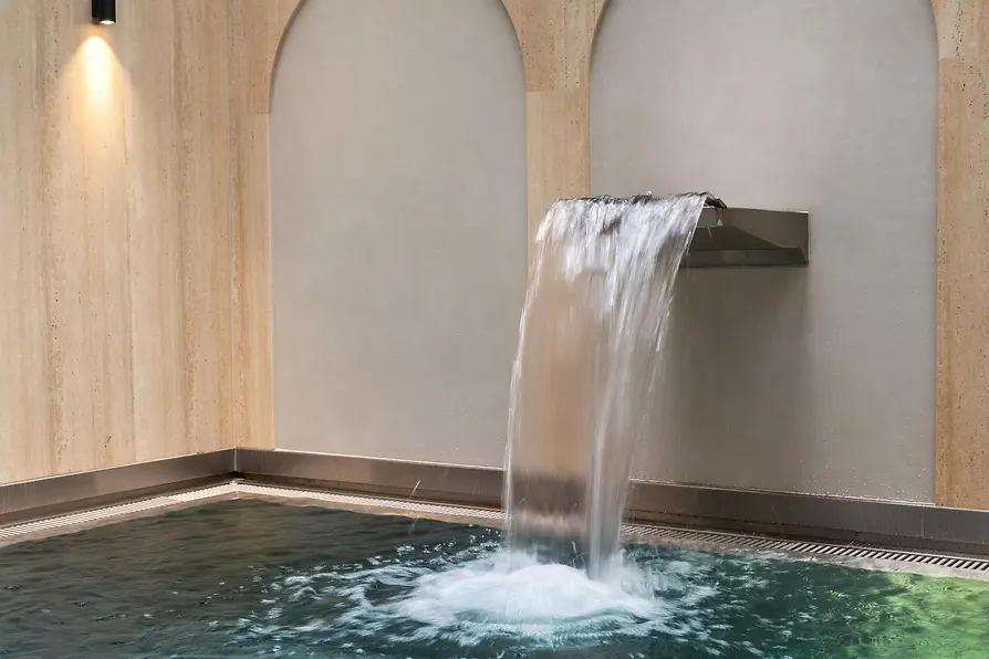 Indoor pool at The Amauris with a waterfall and illuminated wall niches.