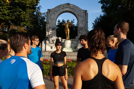 Running group on a city tour in front of a historic archway with a golden statue in Vienna.