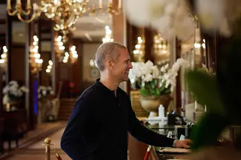 Mann mit Koffer steht an der Rezeption in einem eleganten Hotel um einzuchecken.
