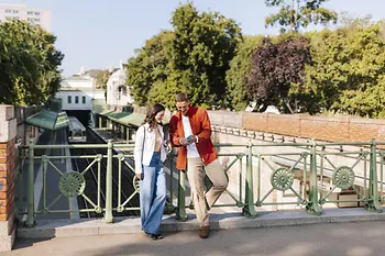 A couple on a bridge in the city park looking at their mobile phone