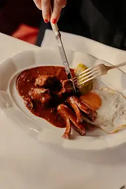 A plate of Fiakergulasch (goulasch) with boiled potatoes, fried egg, and a sausage