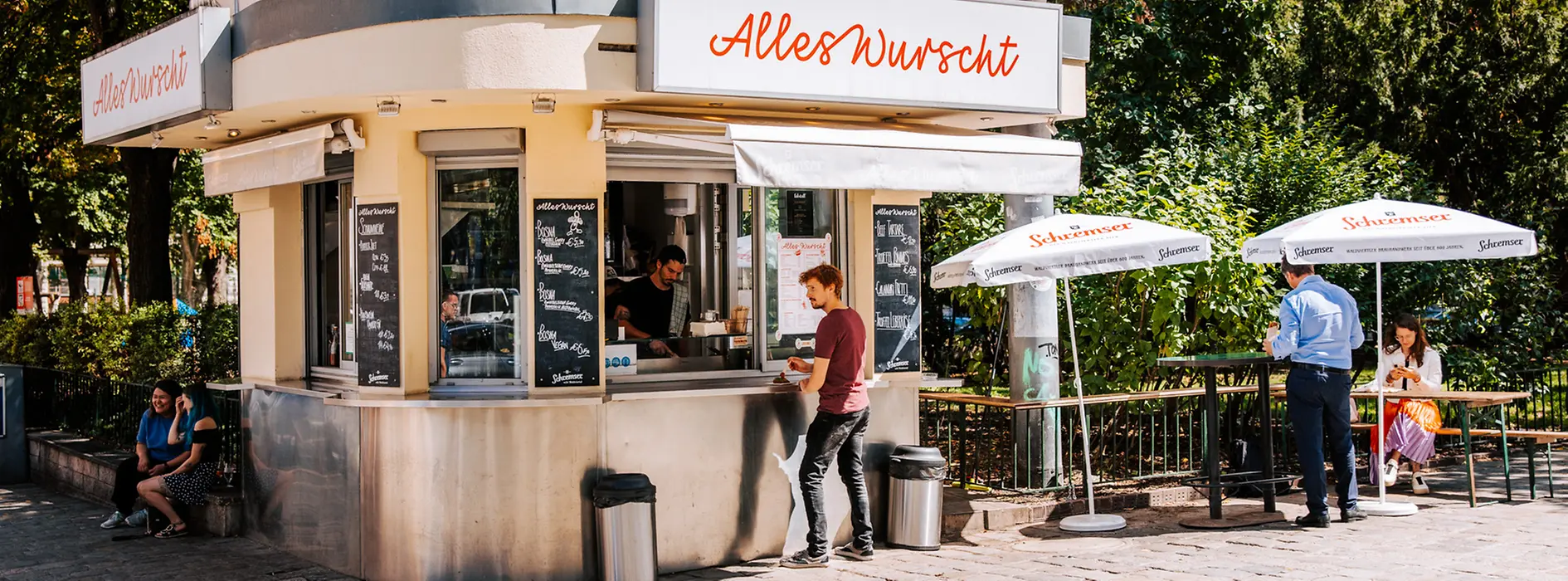 Gäste vor einem Würstelstand mit Sonnenschirmen