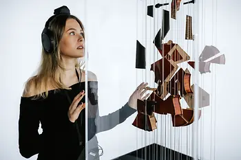 A visitor with headphones marvels at a modern object - a violin hanging in parts from strings.