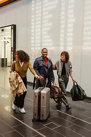 Drei Menschen mit Gepäck im Ankunftsbereich Flughafen Wien