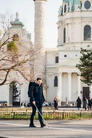 Blinde Person geht mit einem Blindenstock vor der Wiener Karlskirche am Blindenleitsystem entlang