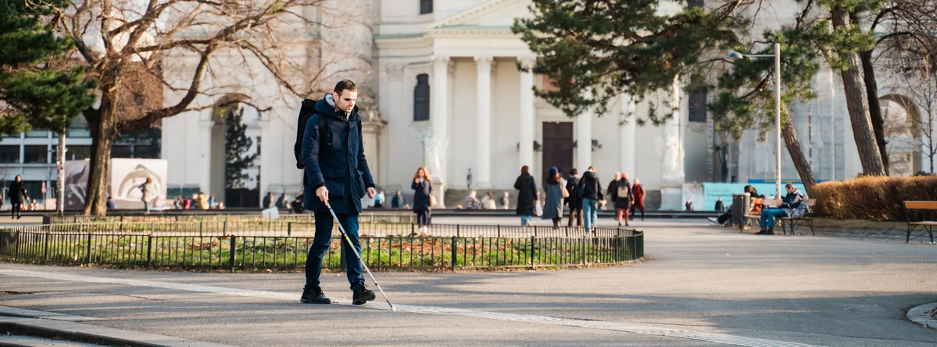 Blind person walks with a cane along the guidance system for the blind in front of St. Charles Church in Vienna