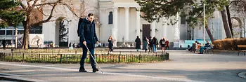 Blind person walks with a cane along the guidance system for the blind in front of St. Charles Church in Vienna