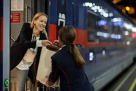 Zugbegleiterin hilft Fahrgast beim Einsteigen in den ÖBB Nightjet mit dem Gepäck